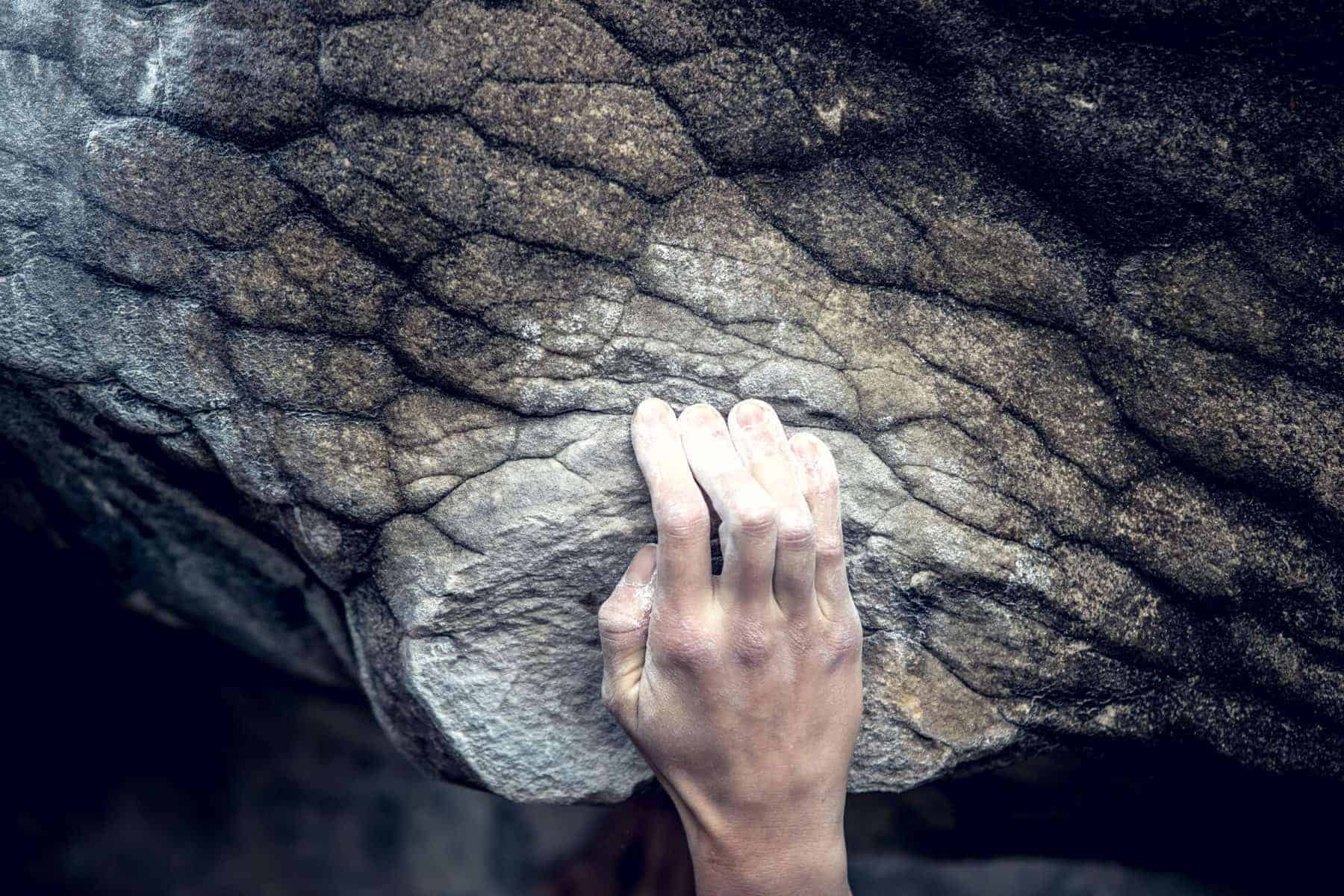 Climber in red t-shirt climbs a gray rock. A strong hand grabbed